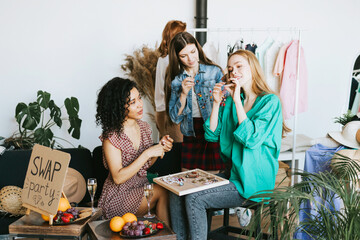 four young woman female caucasian and african students at swap party try on clothes, bags, shoes and accessories, change clothes with each other, second hand for things, zero waste life, eco-friendly