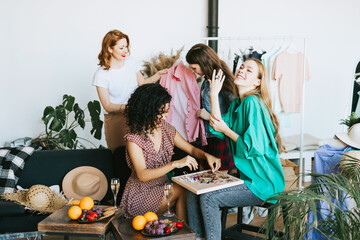 four young woman female caucasian and african students at swap party try on clothes, bags, shoes...