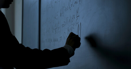 Scientist writing formulas on chalkboard. Hand with chalk wrote physics formulas on black...