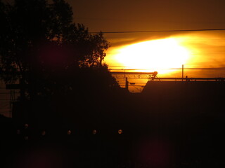 Telephoto closeup of blazing solar sun disc rising over silhouettes of trees and small town...