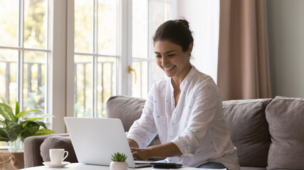 Happy Indian freelancer woman working from home, using laptop computer, calculator, typing, smiling, laughing, chatting online, enjoying business communication. Renter, homeowner using app for payment