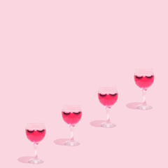 Summer still life scene made with glass, pink cocktail drink, eyelashes and shadows on pastel pink background. Summer vacation refreshment concept.