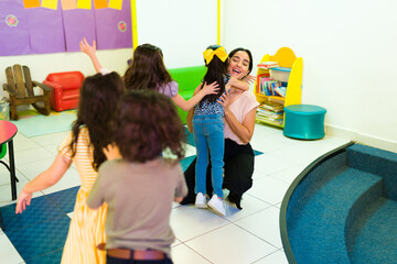 Happy preschool teacher embracing the kids in the classroom