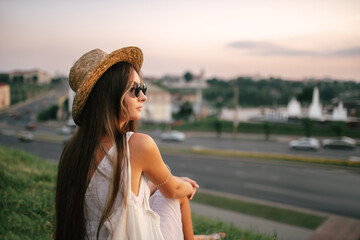 Portrait of a relaxed woman with hat looking forward at the horizon cityscape in the background copy space - 520354341