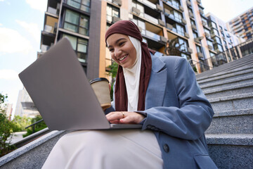 Woman working on a laptop on the street against the backdrop of houses