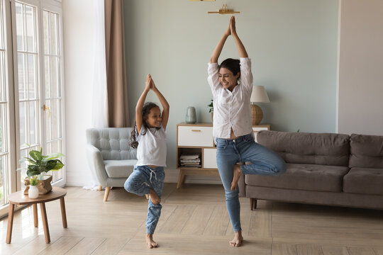 Happy Indian Yogi Mom Teaching Daughter Kid To Do Yoga At Home, Standing In Tree Pose, Smiling, Laughing, Talking, Enjoying Home Exercises, Leisure Activities, Keeping Healthy Life Style