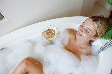 Young beautiful Caucasian woman smiling, lying in bathtub with foam and drinking wine.