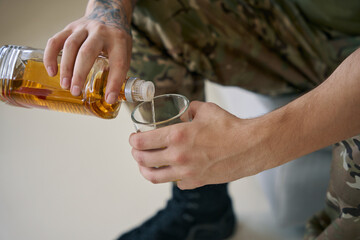 Military person pouring himself glass of whisky