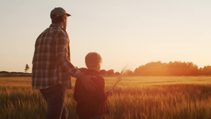 Farmer and his son in front of a sunset agricultural landscape. Man and a boy in a countryside field. Fatherhood, country life, farming and country lifestyle concept.