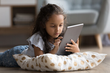 Focused gen Z preteen school kid resting on heating floor with soft pillow, using learning app on...
