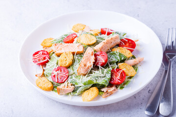 Fototapeta na wymiar Caesar salad with red fish (salmon, trout), cherry tomatoes, croutons, parmesan cheese and romaine. Traditional American dish. Close-up, selective focus.