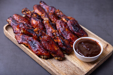 Fried chicken wings on a wooden board with barbecue sauce. Black background, close-up.