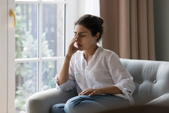 Depressed frustrated young Indian woman suffering from headache, migraine, touching face, head with closed eyes, feeling stressed, sick, tired, thinking over bad news, problems, crisis - Powered by Adobe