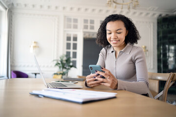 A female designer is working in the office on a new project in a financial company, using a laptop on the desk and a phone