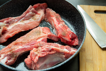 Raw pork ribs are fried in oil in a frying pan