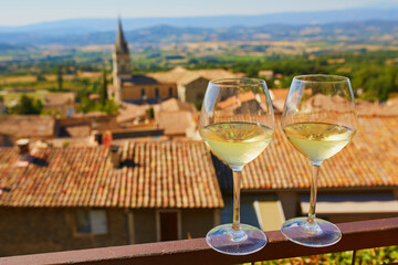 Two glasses of white wine with view to old roofs of Bonnieux village in Provence, France