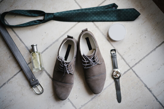 New men's shoes, belt, tie and wristwatch on the floor with a bottle of perfume.