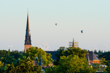 European cathedral tower surrounded by green trees at sunset with hot air balloons. Breda, the...