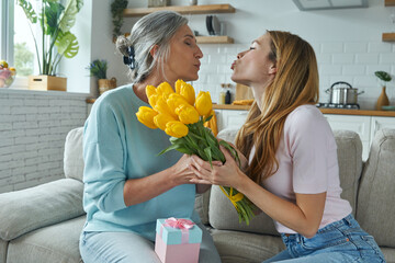 Happy senior woman receiving a gift box and a bunch of tulips from her daughter