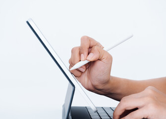 Hand holding white electronic pen or pencil, writing or drawing on digital tablet screen while typing on keyboard computer isolated on white background, side view. Work with technology.