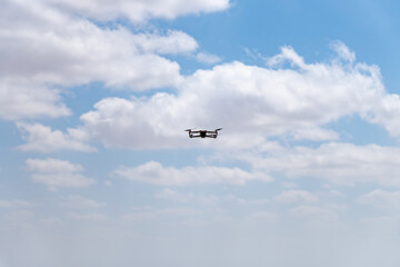 Small grey drone in blue sky with clouds