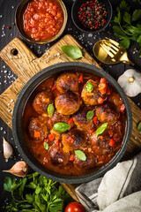 Meatballs in tomato sauce in a skillet on dark kitchen table with ingredients. Top view with copy space.