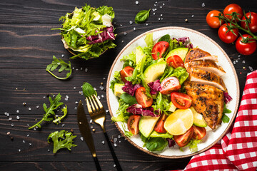 Healthy food concept. Diet menu. Grilled chicken with fresh salad. Top view at dark wooden table.