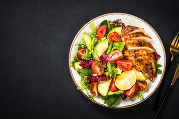 Healthy food concept. Grilled chicken with fresh salad at black background. Top view with copy...