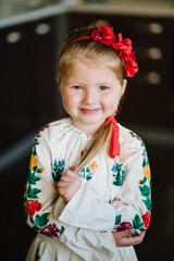 Portrait of a cute girl dressed in Ukrainian folk embroidered dress posing for a photo. Child with wreath of poppies on his head at home. National ethnic traditional costume or dress.