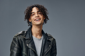 Obraz premium Cheerful smiling stylish tanned curly man leather jacket posing isolated on over gray studio background. Cool fashion offer. Huge Seasonal Sale New Collection concept. Copy space for ad