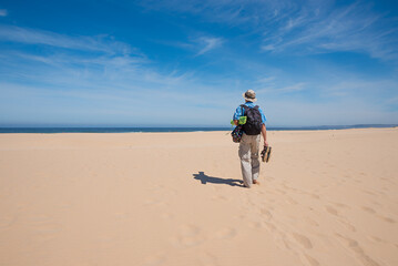 man walking over the sandy beach towards the blue ocean