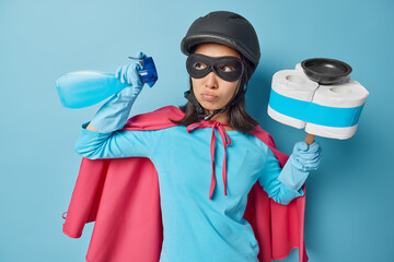 Photo of serious woman with dark hair dressed in superhero costume holds spray detergent and...