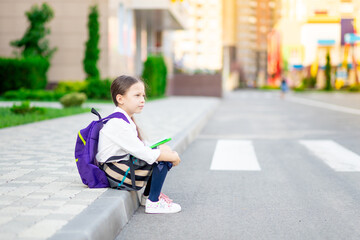 a first-grader girl with a backpack and a book in her hands at the school is reading a book or doing homework, the concept is back to school