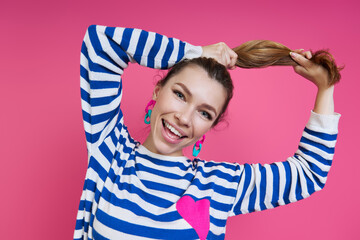 Beautiful young woman adjusting hair and smiling while standing against colored background
