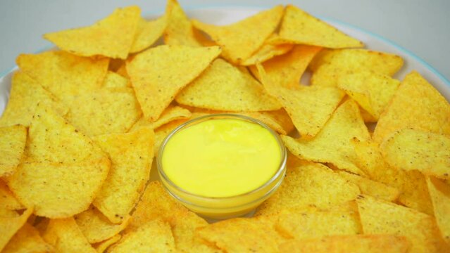 The girl's hand holds nachos with cheese sauce over a plate. Close-up of torilla chili. mexican food
