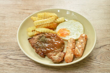 grilled pork steak dressing gravy sauce with french fries and fried egg couple sausage on plate  