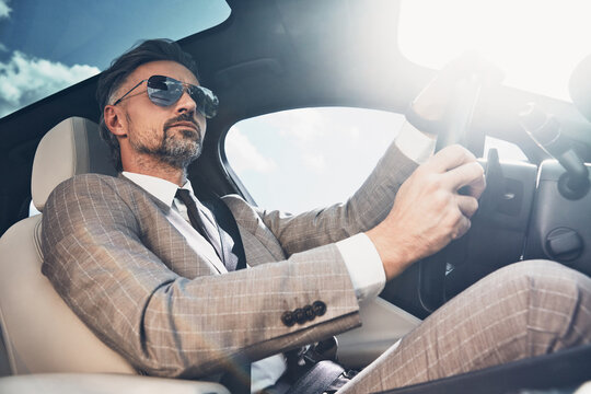 Low angle view of good looking mature man in formalwear driving a car