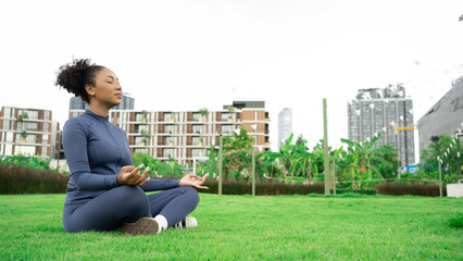 Young african american woman meditating in nature.Attractive sporty black woman doing warming up stretching exercses on yoga mat at urban park, copy space. Positive African American lady work out. - obrazy, fototapety, plakaty
