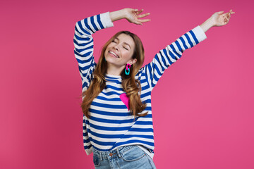 Happy young woman keeping arms outstretched while standing against colored background