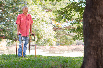 Happy old elderly Asian man uses a walker and walks in the Park.  Concept of happy retirement With care from a caregiver and Savings and senior health insurance
