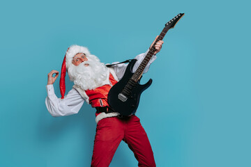 Emotional Santa musician plays on electric guitar on blue background. Christmas music New Year party