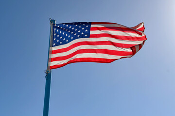 Fototapeta premium National American flag, the Stars and Stripes, backlit agianst a blue sky. No people.