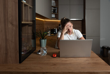 Young stressed student or freelancer business woman having anxiety attack and migraine from bad internet connection while she working online on her laptop computer in home office. - obrazy, fototapety, plakaty