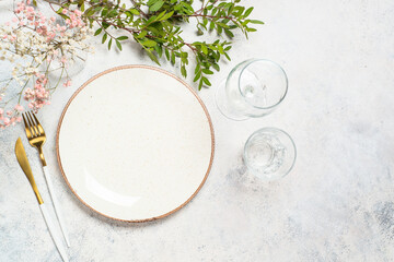Spring or summer table setting with plate, flowers and cutlery at white kitchen table. Top view.