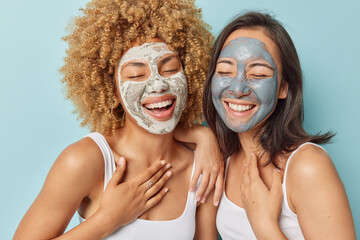 Joyful two young women with different appearance apply beauty masks smile gladfully dressed...