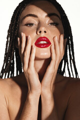 Vertical shot of sexual woman with red lipstick, touches her face and looks sensual at camera, has...