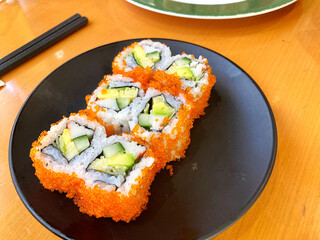 portrait of japanese cuisine, california maki sushi on black plate.