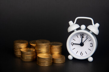 White alarm clock with gold coins isolated on dark background. Copy space and business concept