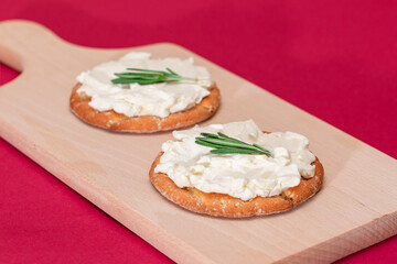 Crispy Cracker Sandwich with Cream Cheese and Rosemary on Wooden Cooking Board on Magenta Background