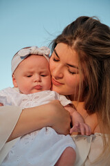 a beautiful girl in a white dress with a newborn baby is sitting on the beach, on the sand.
